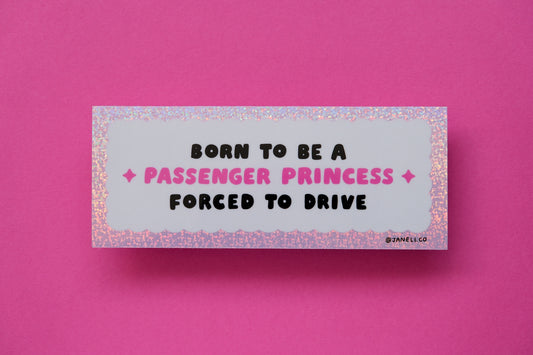 Photo of a glittery pink and white bumper sticker that says "Born to be a passenger princess, forced to drive" over a pink background.