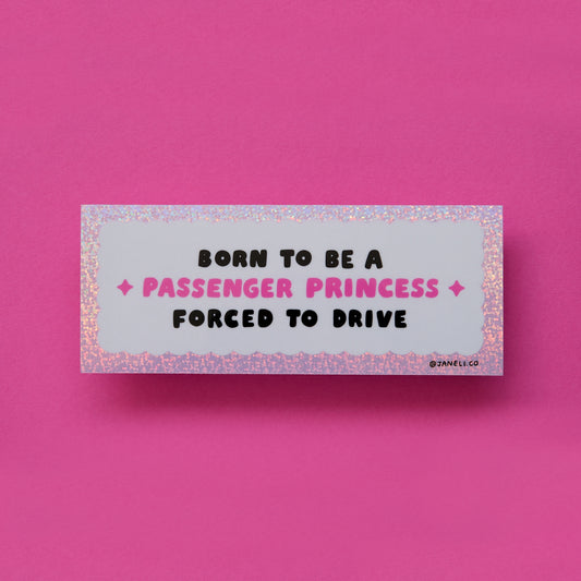 Photo of a glittery pink and white bumper sticker that says "Born to be a passenger princess, forced to drive" over a pink background.