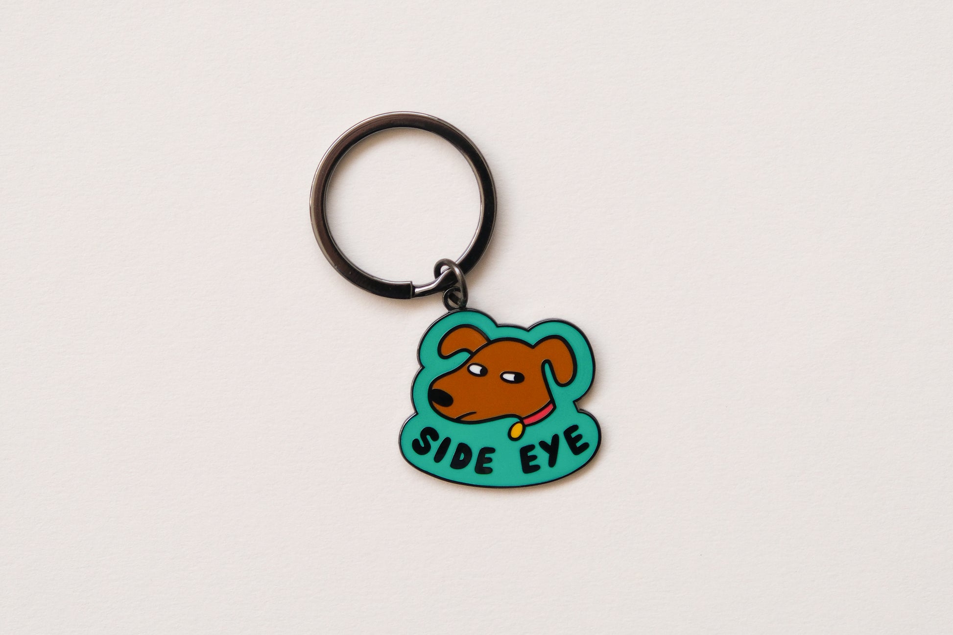 An enamel keychain showing a sassy dog giving side eye that says "Side Eye" over a cream background.