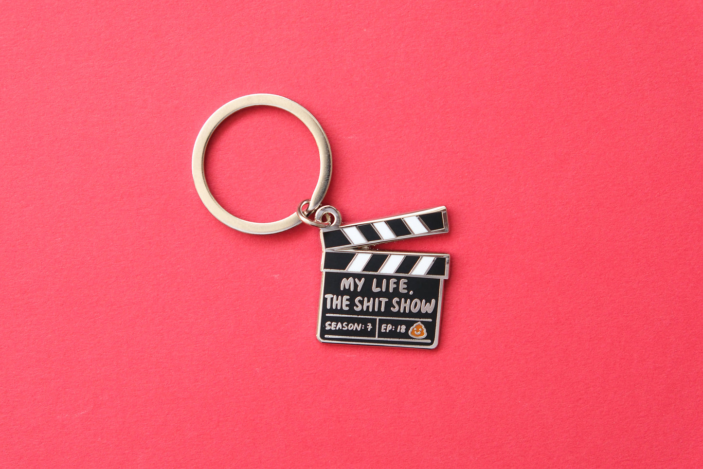 An enamel keychain showing a movie clapper that says "My Life, the Shit Show" over a red background.