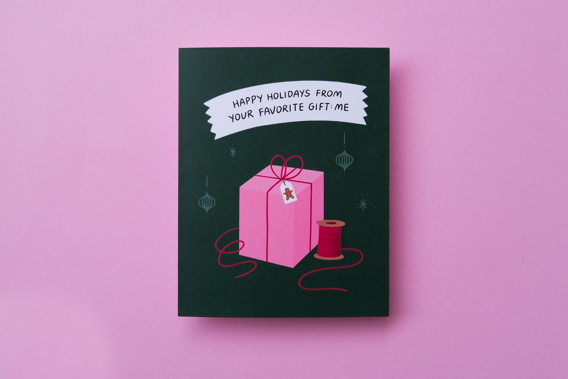 A photo of a greeting card that says "Happy Holidays From Your Favorite Gift: Me" with a presenton a pink background.