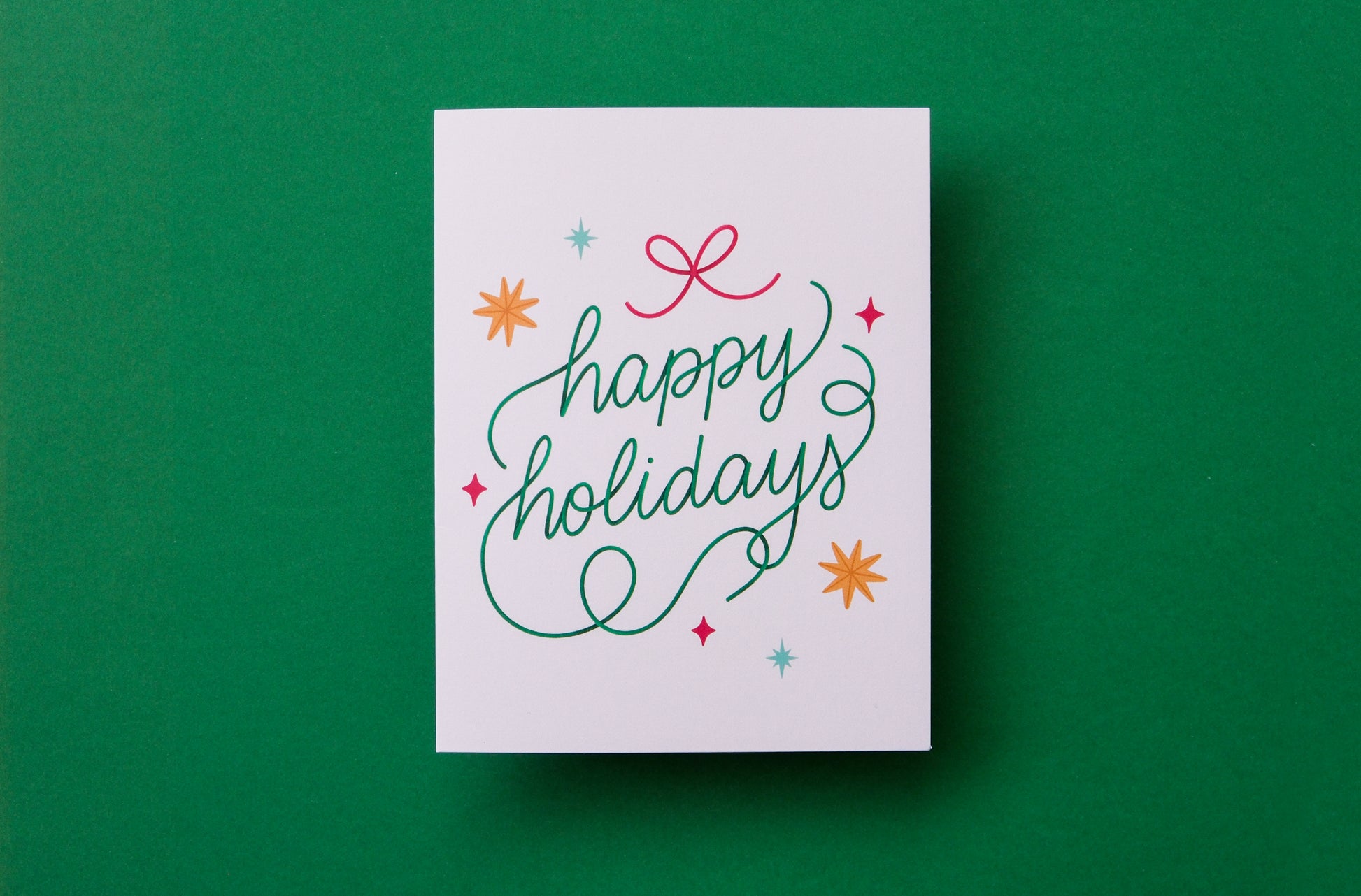 A photo of a greeting card that says "happy holidays" with stars and a bow on a green background.