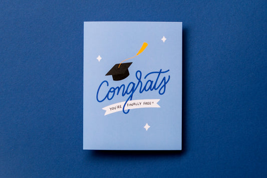 A photo of a greeting card that says "Congrats you're finally free!!" with a graduation cap on a dark blue background.