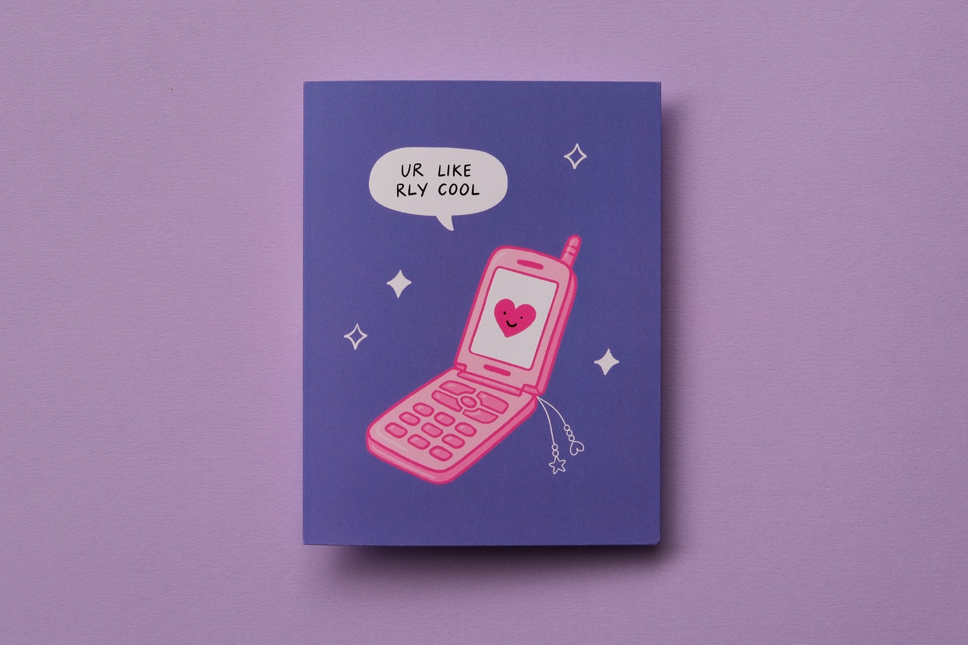 A photo of a greeting card that says "ur like rly cool" with a pink retro flip phone on a lavender background.
