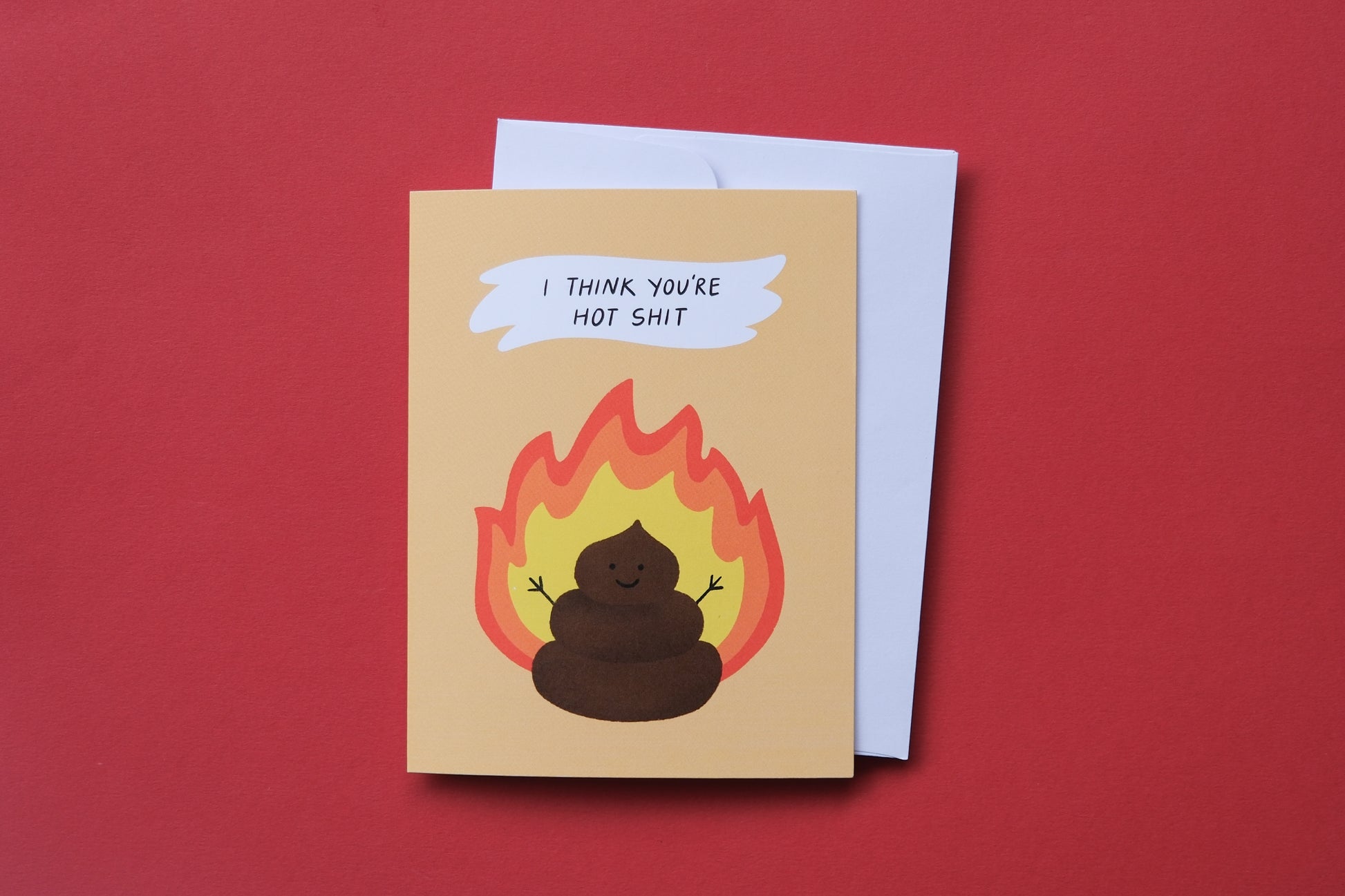 A photo of a greeting card with a flaming poop that says "I think you're hot shit" and a white envelope on a red background.
