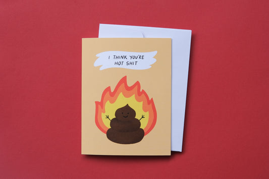 A photo of a greeting card with a flaming poop that says "I think you're hot shit" and a white envelope on a red background.