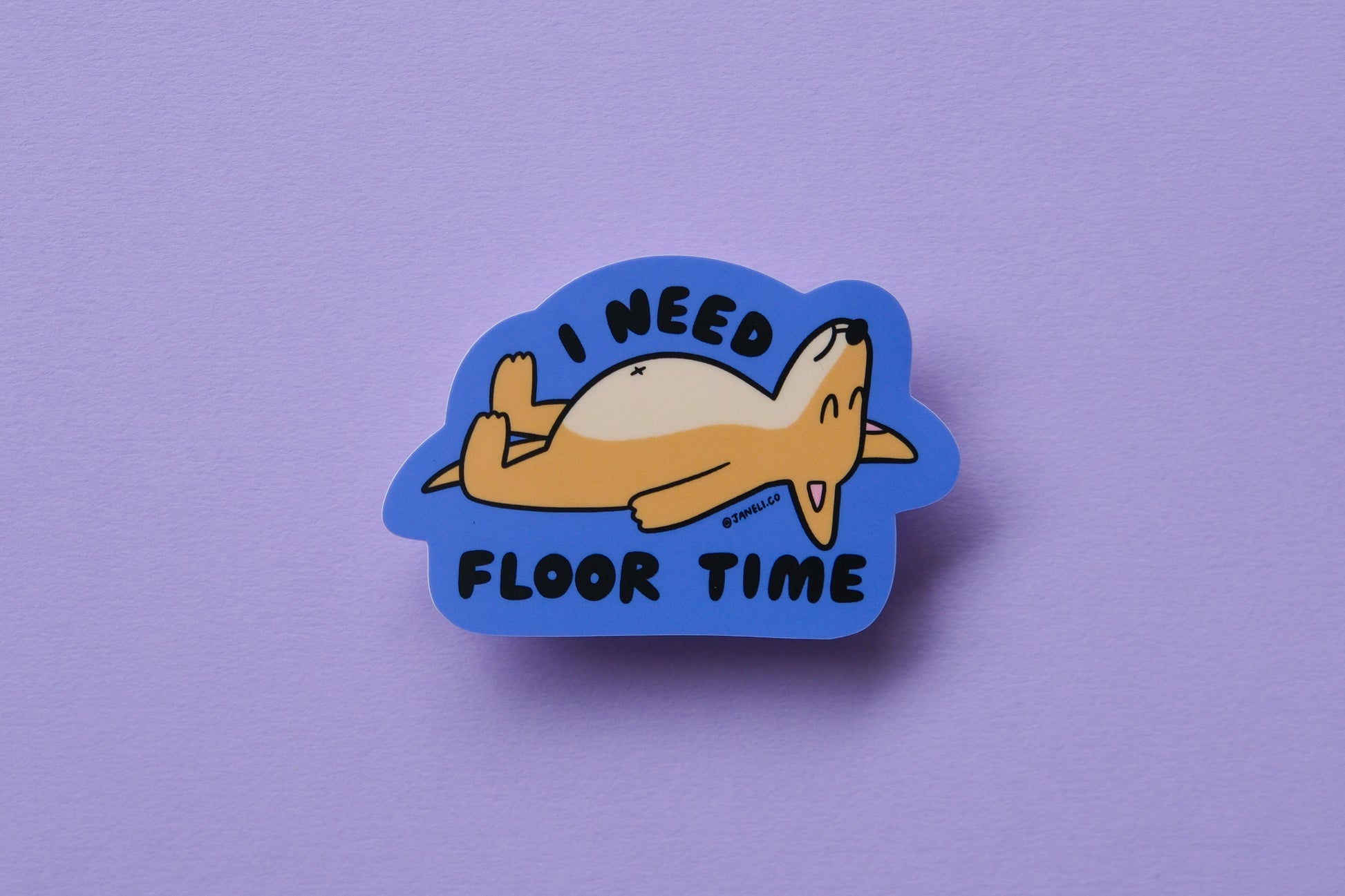 A JaneLi.Co sticker of a dog lying on the floor that says "I need floor time" over a lavender background.