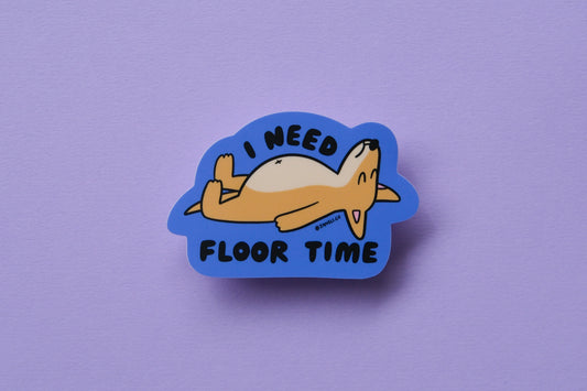 A JaneLi.Co sticker of a dog lying on the floor that says "I need floor time" over a lavender background.