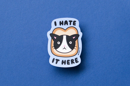 A JaneLi.Co sticker of a cat stuck in a slice of bread that says "I hate it here" over a blue background.