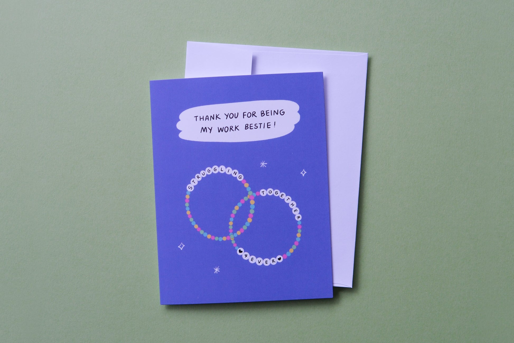 A photo of a greeting card that says "Thank you for being my work bestie!" with two friendship bracelets and a white envelope on a light green background.