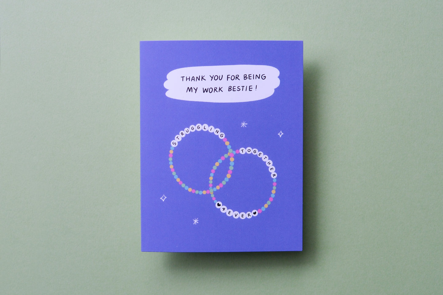 A photo of a greeting card that says "Thank you for being my work bestie" with two friendship bracelets on a light green background.