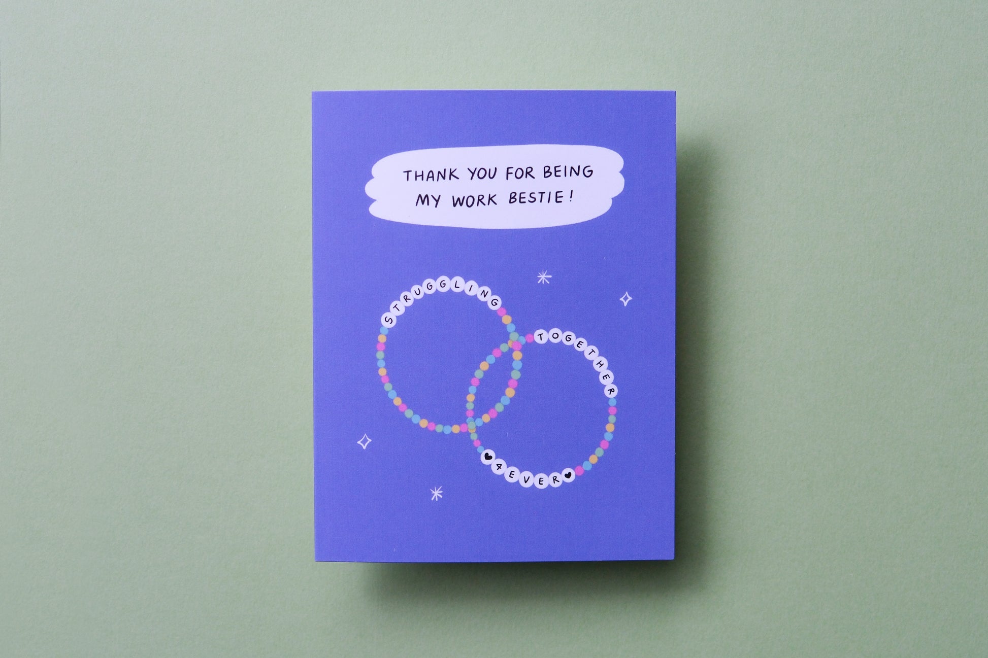 A photo of a greeting card that says "Thank you for being my work bestie" with two friendship bracelets on a light green background.