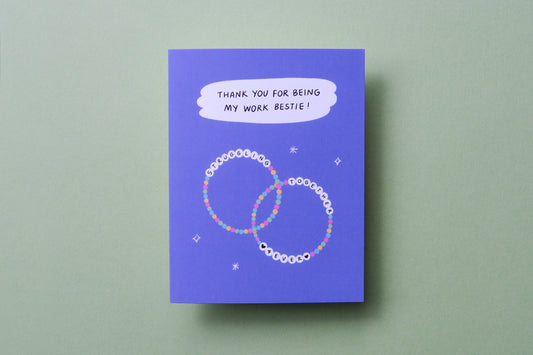 A photo of a greeting card that says "Thank you for being my work bestie" with two friendship bracelets on a light green background.