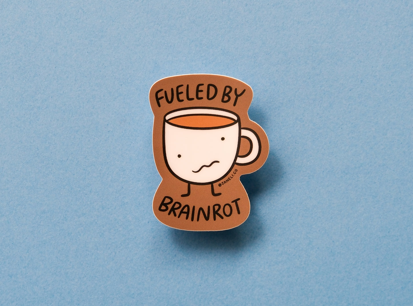 A JaneLi.Co sticker of a wonky coffee mug that says "Fueled by brainrot" over a blue background.