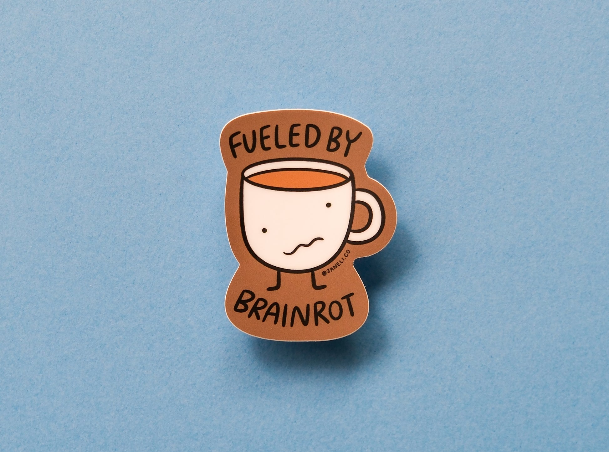 A JaneLi.Co sticker of a wonky coffee mug that says "Fueled by brainrot" over a blue background.