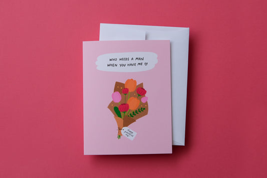 A photo of a greeting card a bouquet of flowers with a tag that says "Happy Galentine's Day" and "Who needs a man when you have me" over a white envelope on a pink background.