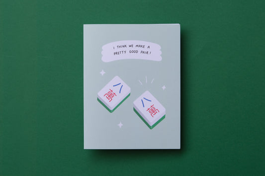 A photo of a greeting card with a pair of matching mahjong tiles "I think we make a pretty good pair!" and a white envelope on a green background.