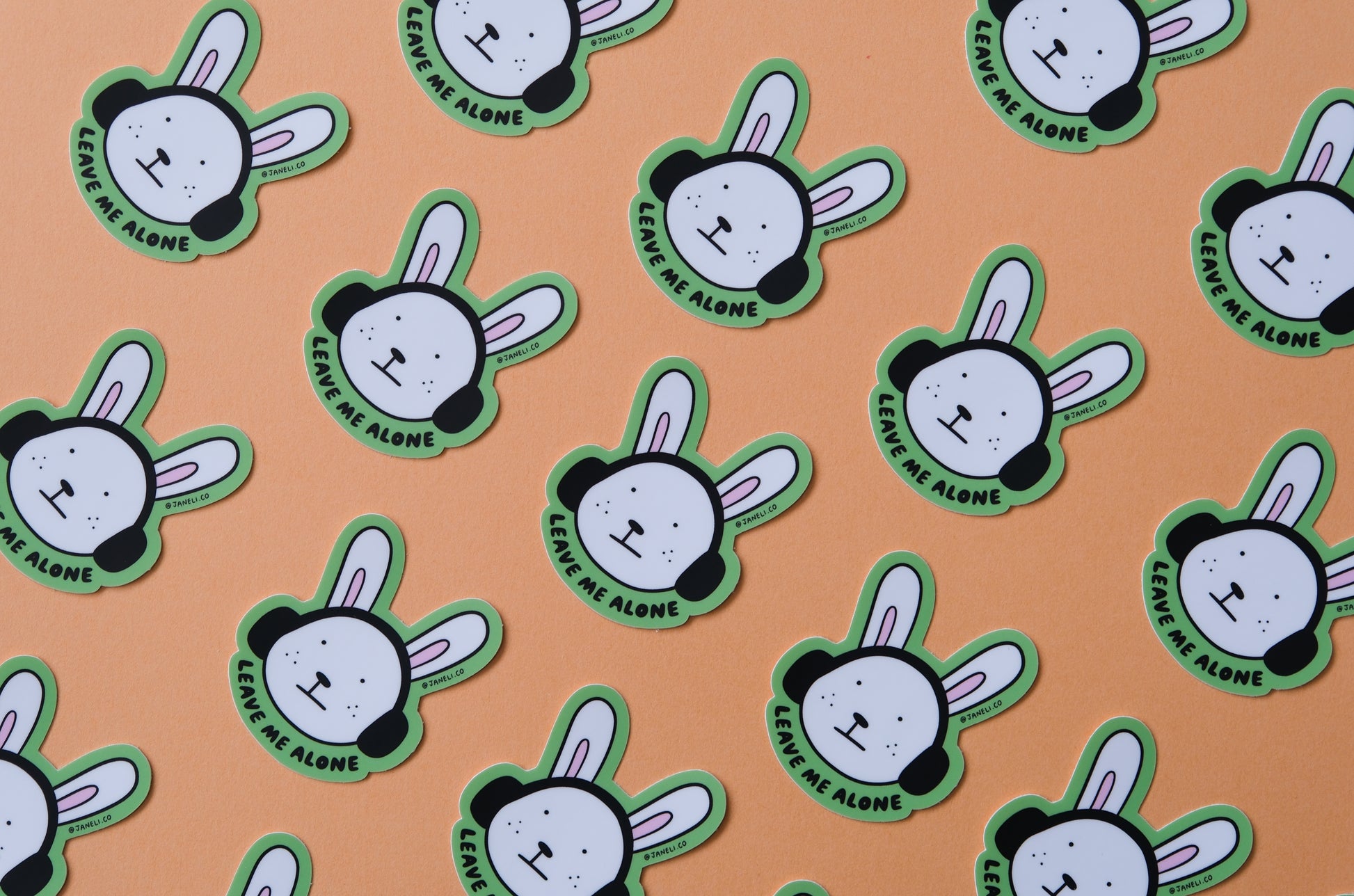 A grid of JaneLi.Co stickers of bunnies with headphones on that says "Leave me alone" over an orange background.