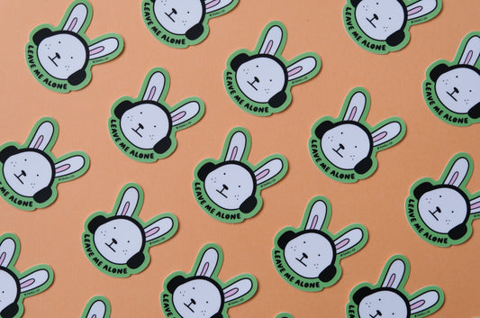 A grid of JaneLi.Co stickers of bunnies with headphones on that says "Leave me alone" over an orange background.