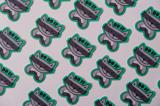 A grid of JaneLi.Co stickers of evil raccoons that say "Do it" over an cream background.