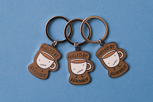 3 enamel keychains of wonky coffee mugs that say "Fueled by brainrot" over a blue background.