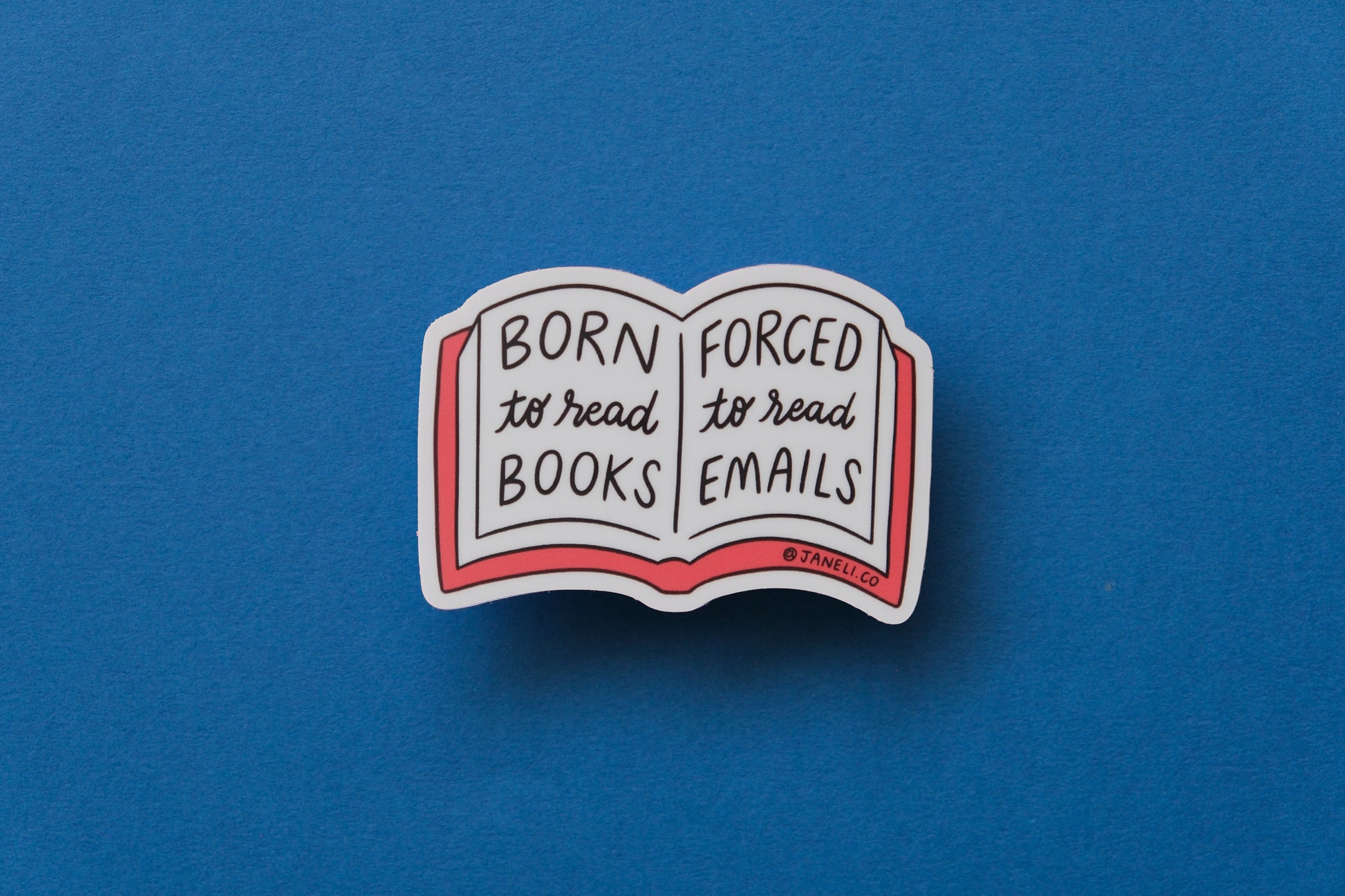 A JaneLi.Co sticker of an open book that says "Born to read books, forced to read emails" over a blue background.