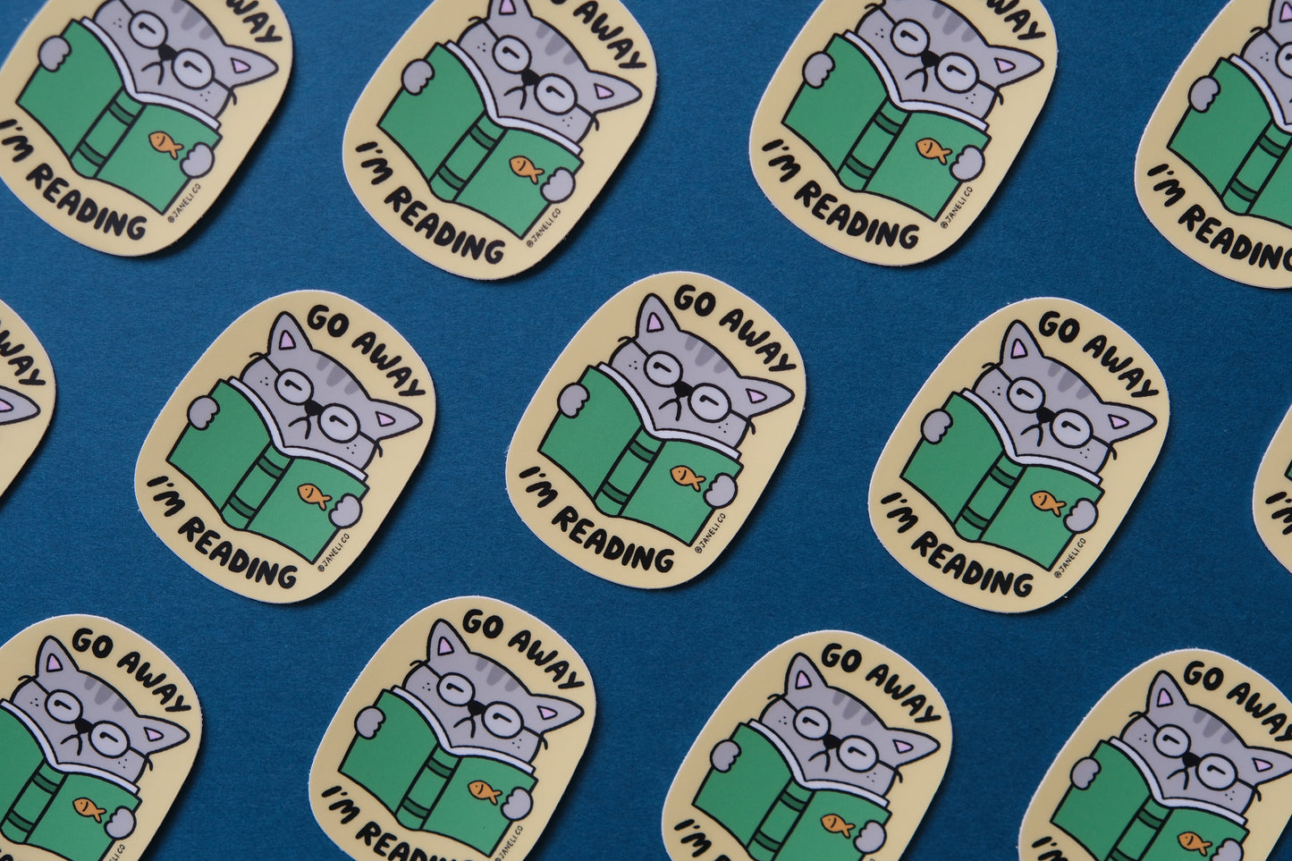 A grid of JaneLi.Co stickers of cats reading books that say "Go Away I'm Reading" over a teal background.