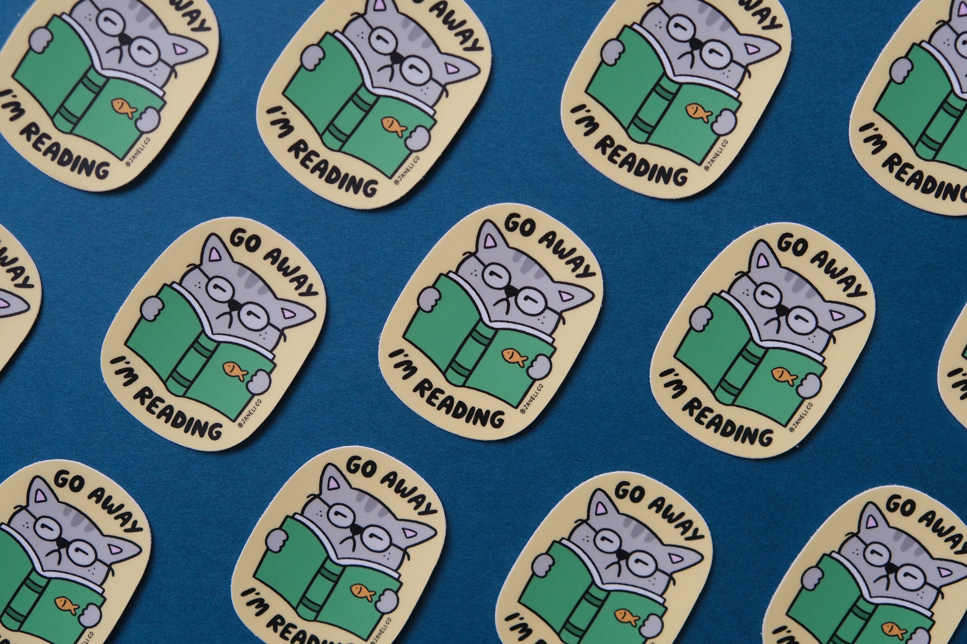 A grid of JaneLi.Co stickers of cats reading books that say "Go Away I'm Reading" over a teal background.