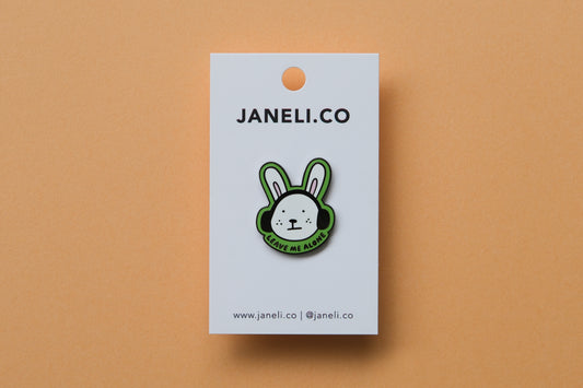 An enamel pin of a rabbit wearing headphones that says "Leave me alone" over an orange background.
