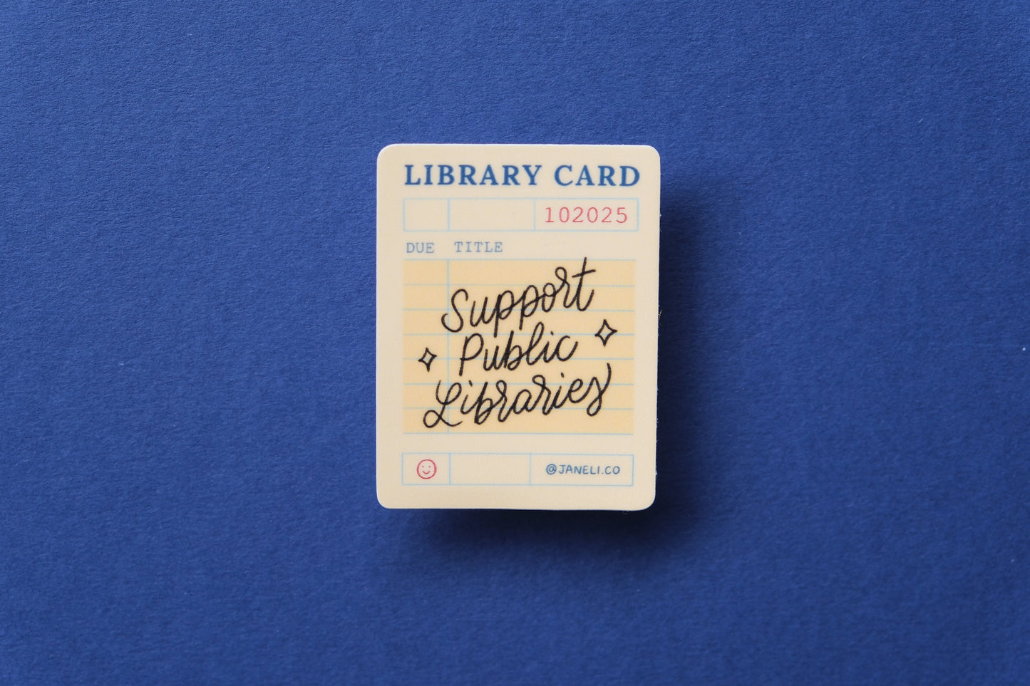 A JaneLi.Co sticker of a vintage library card that says "Support Public Libraries" over a dark blue background.