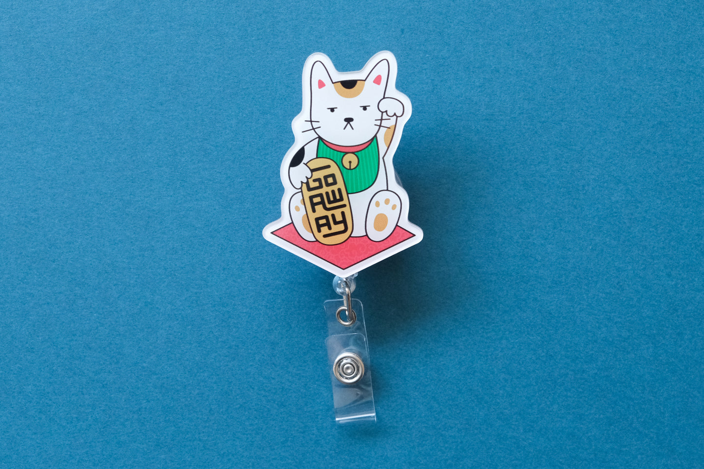 Photo of an acrylic badge reel shaped like a beckoning cat that says "Go Away" over a teal background.