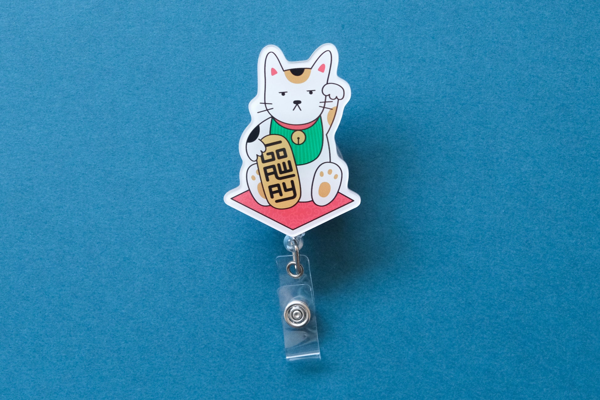Photo of an acrylic badge reel shaped like a beckoning cat that says "Go Away" over a teal background.