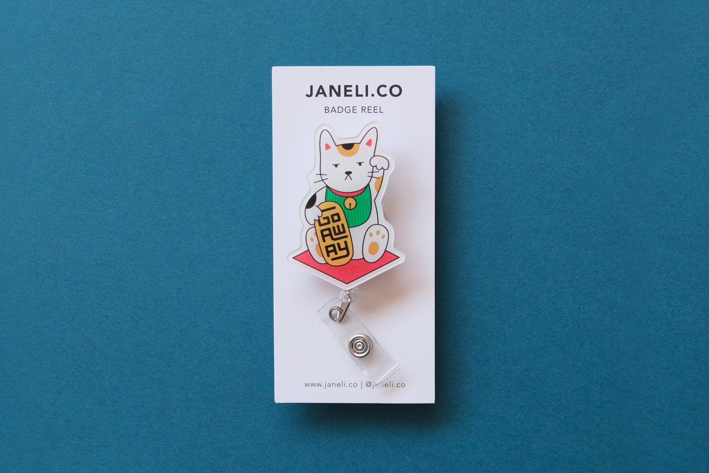 Photo of an acrylic badge reel shaped like a beckoning cat that says "Go Away" on a white backing card over a teal background.