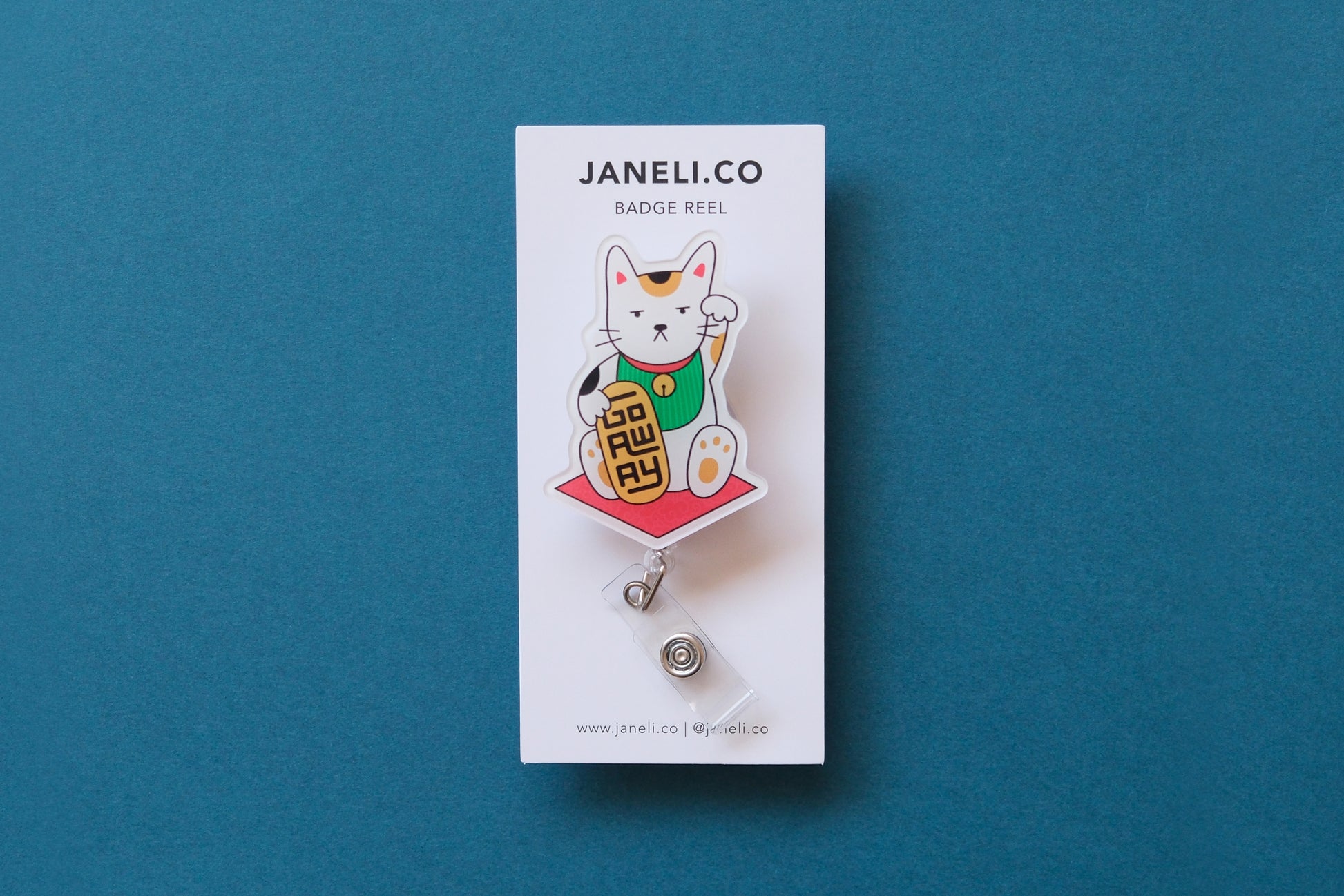 Photo of an acrylic badge reel shaped like a beckoning cat that says "Go Away" on a white backing card over a teal background.