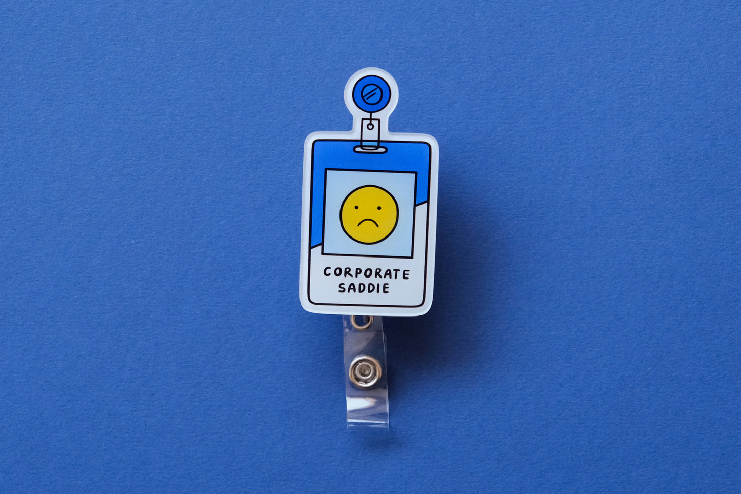 Photo of an acrylic badge reel shaped like a corporate badge that says "Corporate Saddie" over a dark blue background.