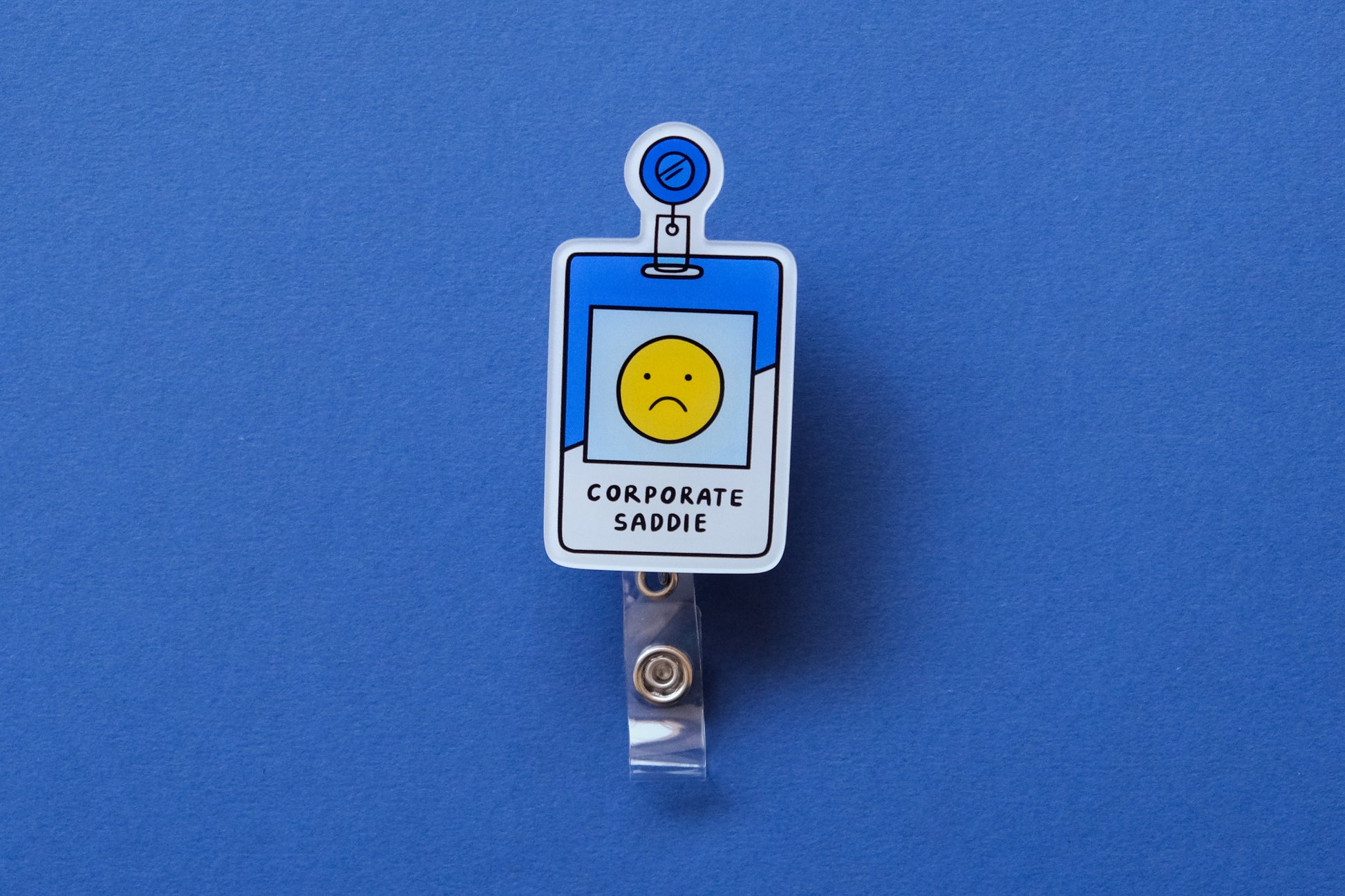 Photo of an acrylic badge reel shaped like a corporate badge that says "Corporate Saddie" over a dark blue background.