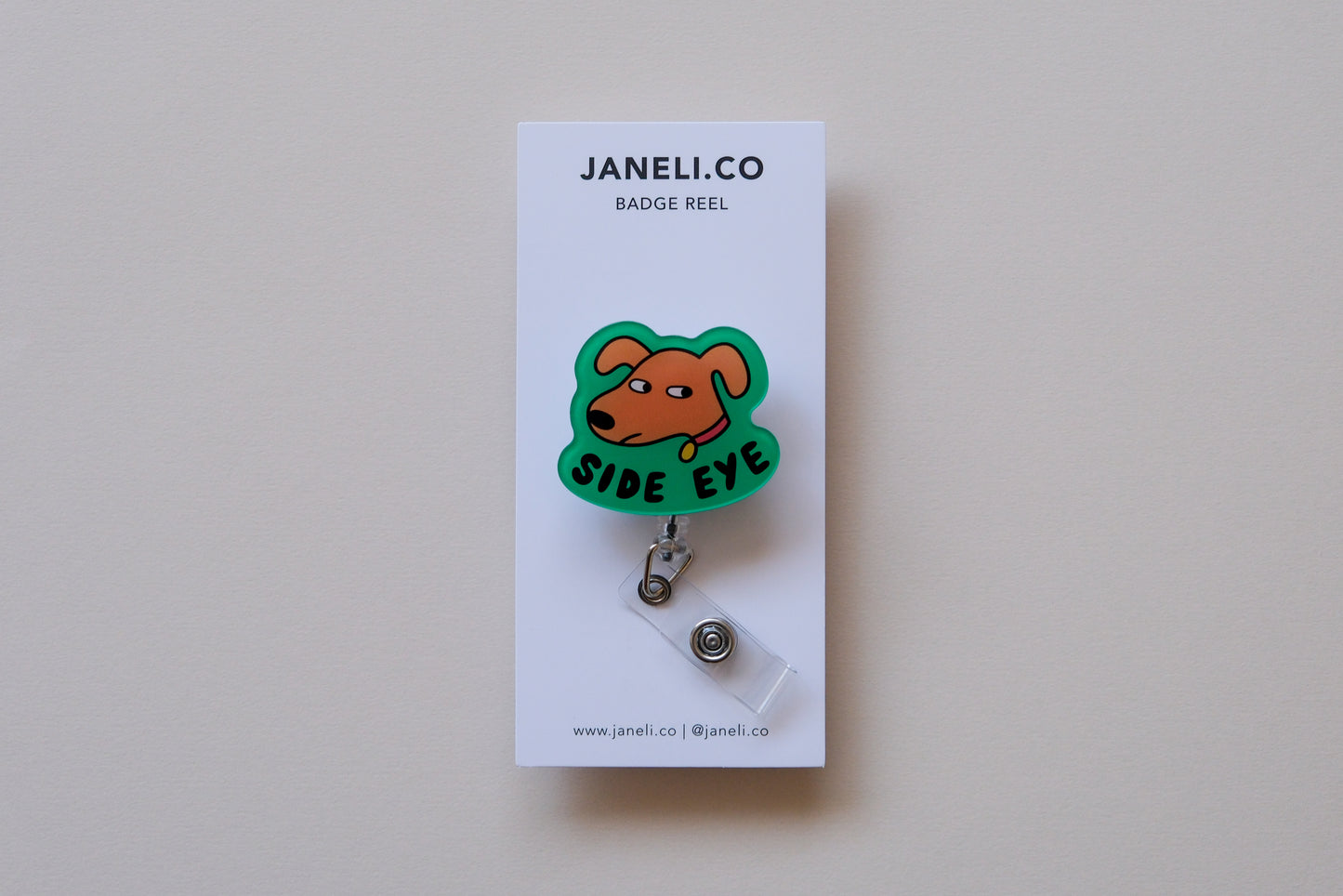 Photo of an acrylic badge reel shaped like a dog that says "Side Eye" on a white backing card over a cream background.