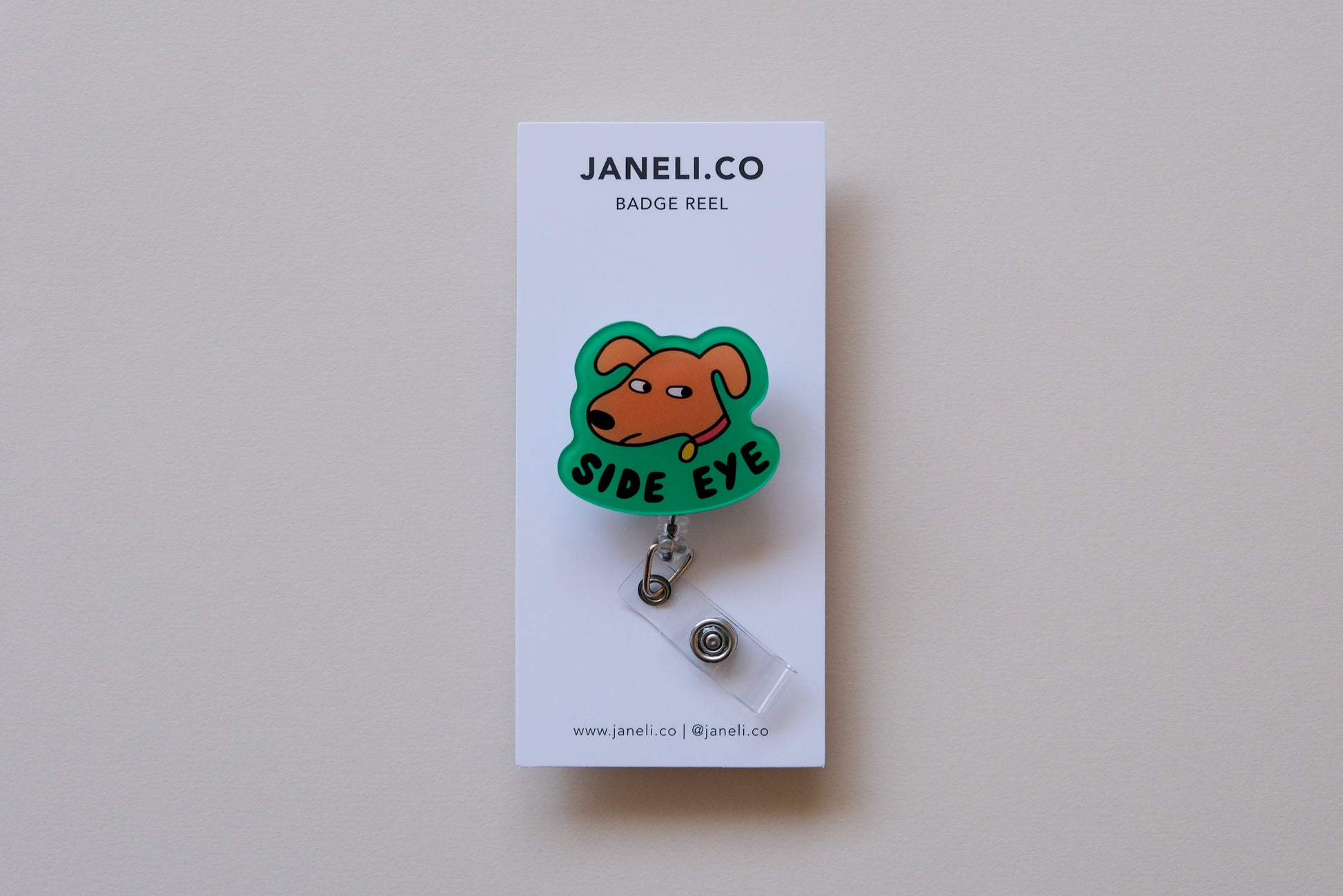 Photo of an acrylic badge reel shaped like a dog that says "Side Eye" on a white backing card over a cream background.