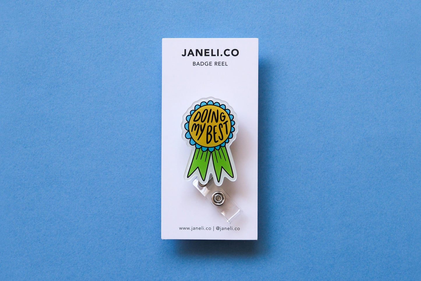Photo of an acrylic badge reel shaped like an award ribbon that says "Doing My Best" on a white backing card over a light blue background.
