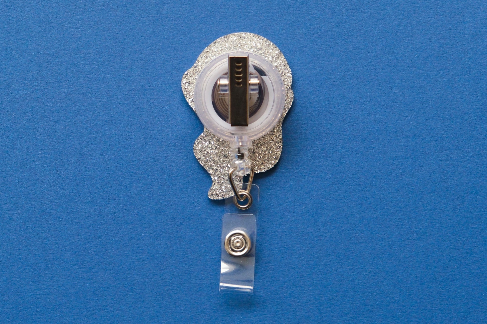 Photo of the back of an acrylic badge reel with an alligator clip over a dark blue background.
