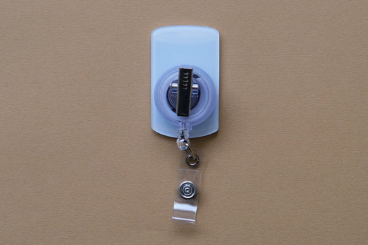 Photo of the back of an acrylic badge reel with an alligator clip over a tan background.