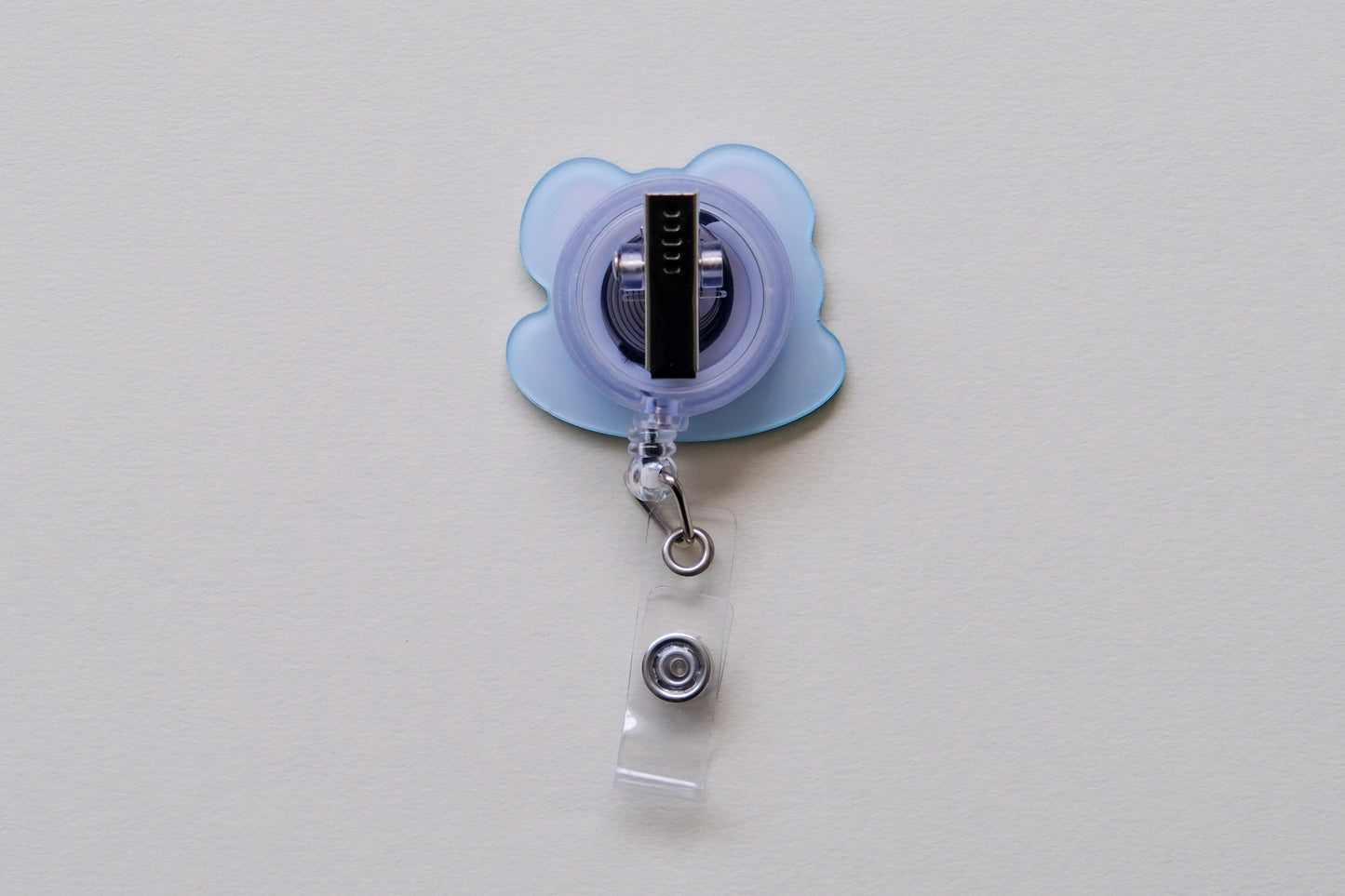 Photo of the back of an acrylic badge reel with an alligator clip over a cream background.