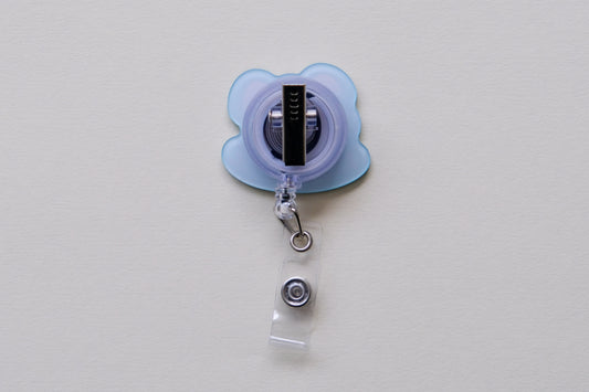 Photo of the back of an acrylic badge reel with an alligator clip over a cream background.