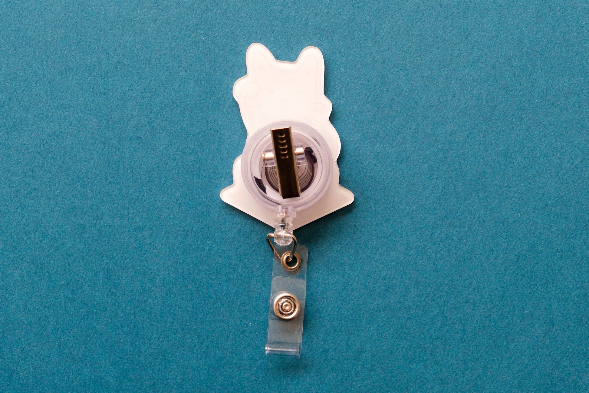 Photo of the back of an acrylic badge reel with an alligator clip over a teal background.