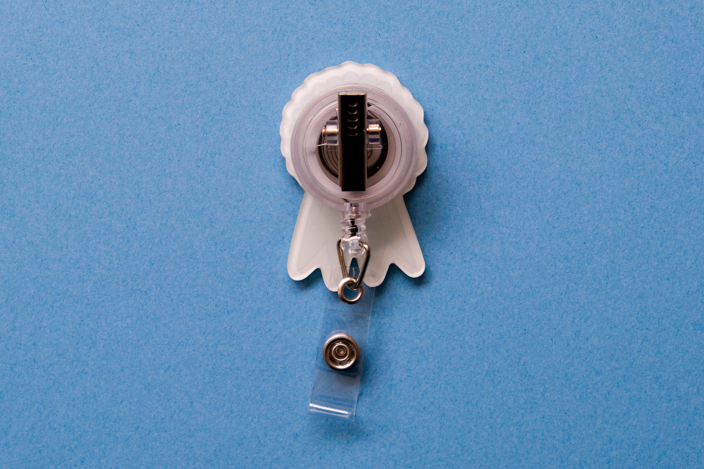 Photo of the back of an acrylic badge reel with an alligator clip over a light blue background.