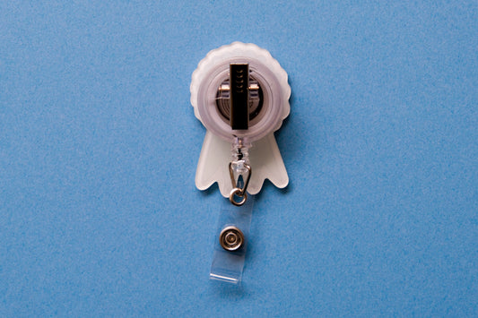 Photo of the back of an acrylic badge reel with an alligator clip over a light blue background.