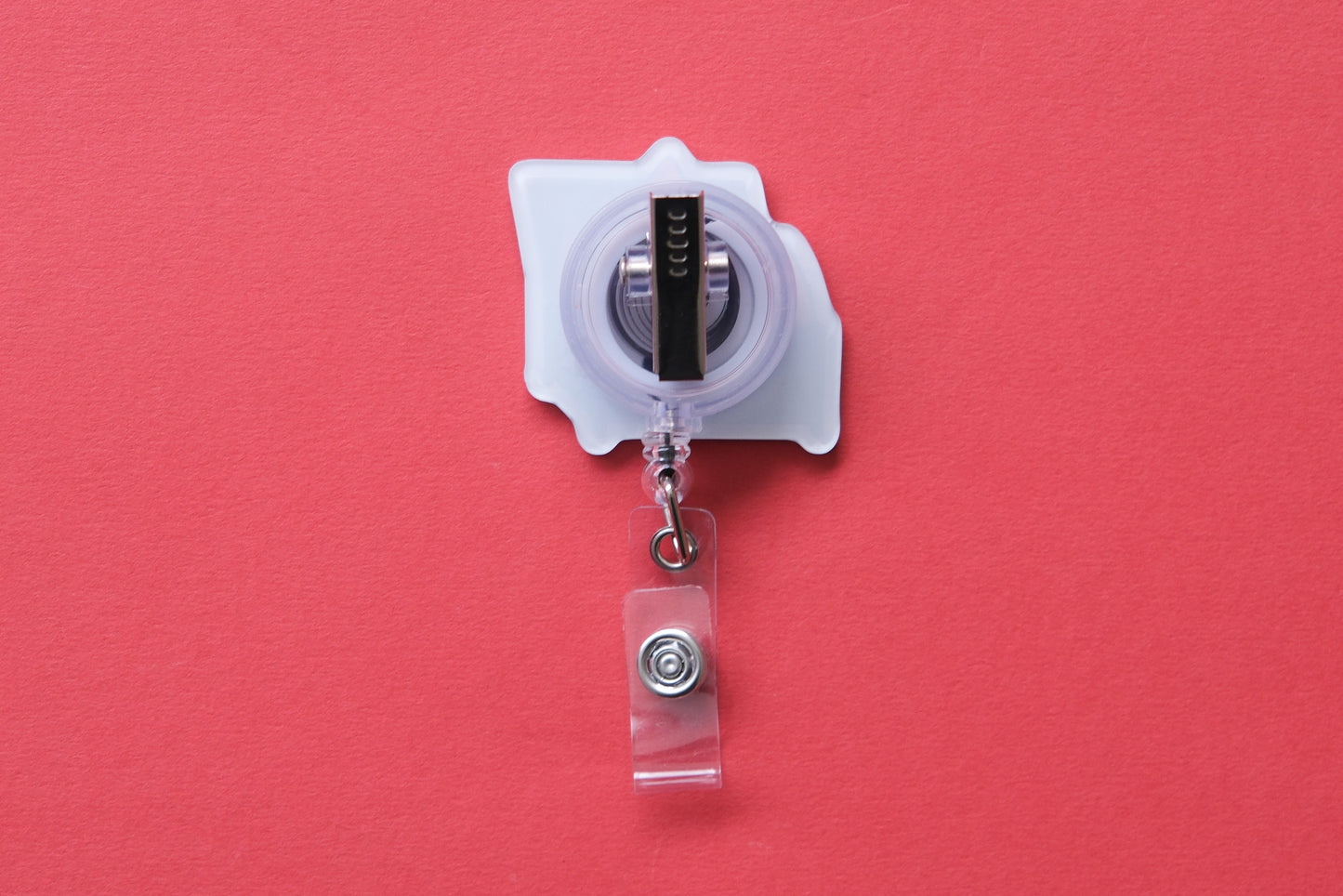 Photo of the back of an acrylic badge reel with an alligator clip over a red background.