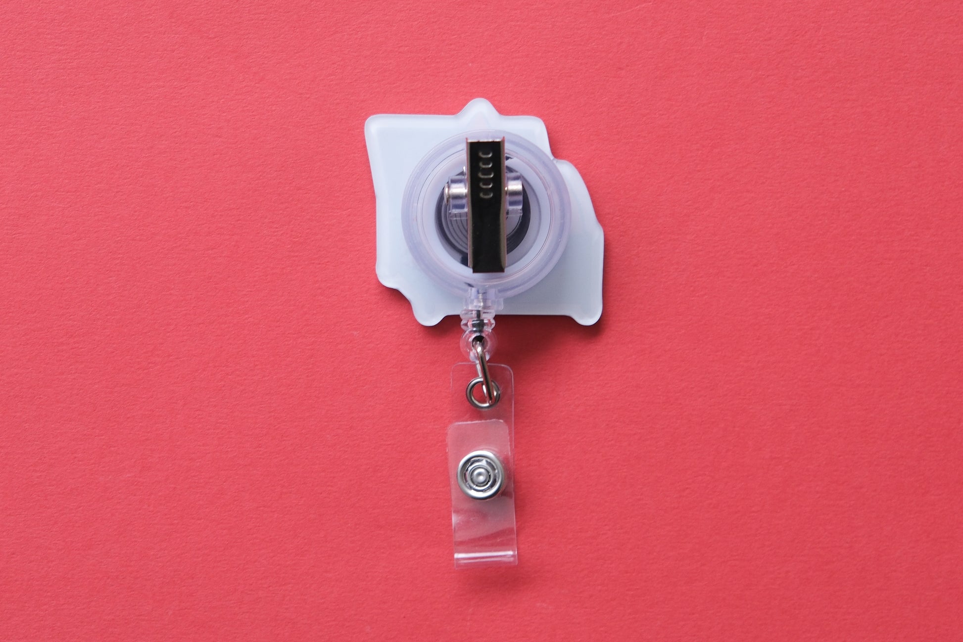 Photo of the back of an acrylic badge reel with an alligator clip over a red background.