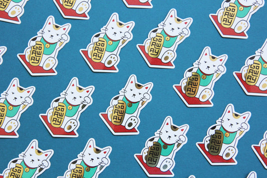 A grid of JaneLi.Co stickers that show Maneki Neko cats holding a metallic gold bars that say "Go Away" over a teal background.