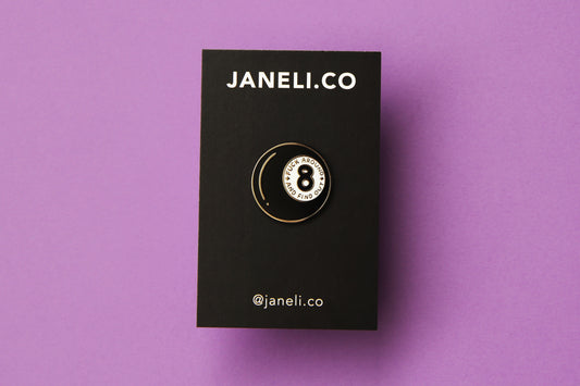 An enamel pin showing a magic 8 ball that says "Fuck around and find out" on a black JaneLi.Co backing card over a purple background.